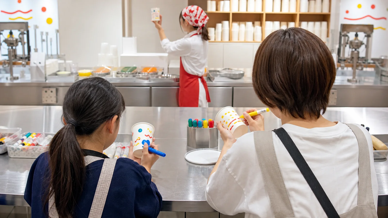 インスタント麺の体験展示で紙カップに絵を描く親子