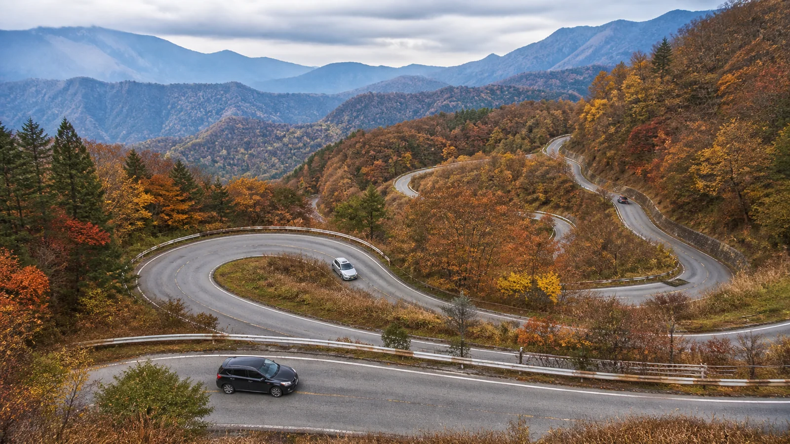 紅葉した山を縫う複数のヘアピンカーブと車
