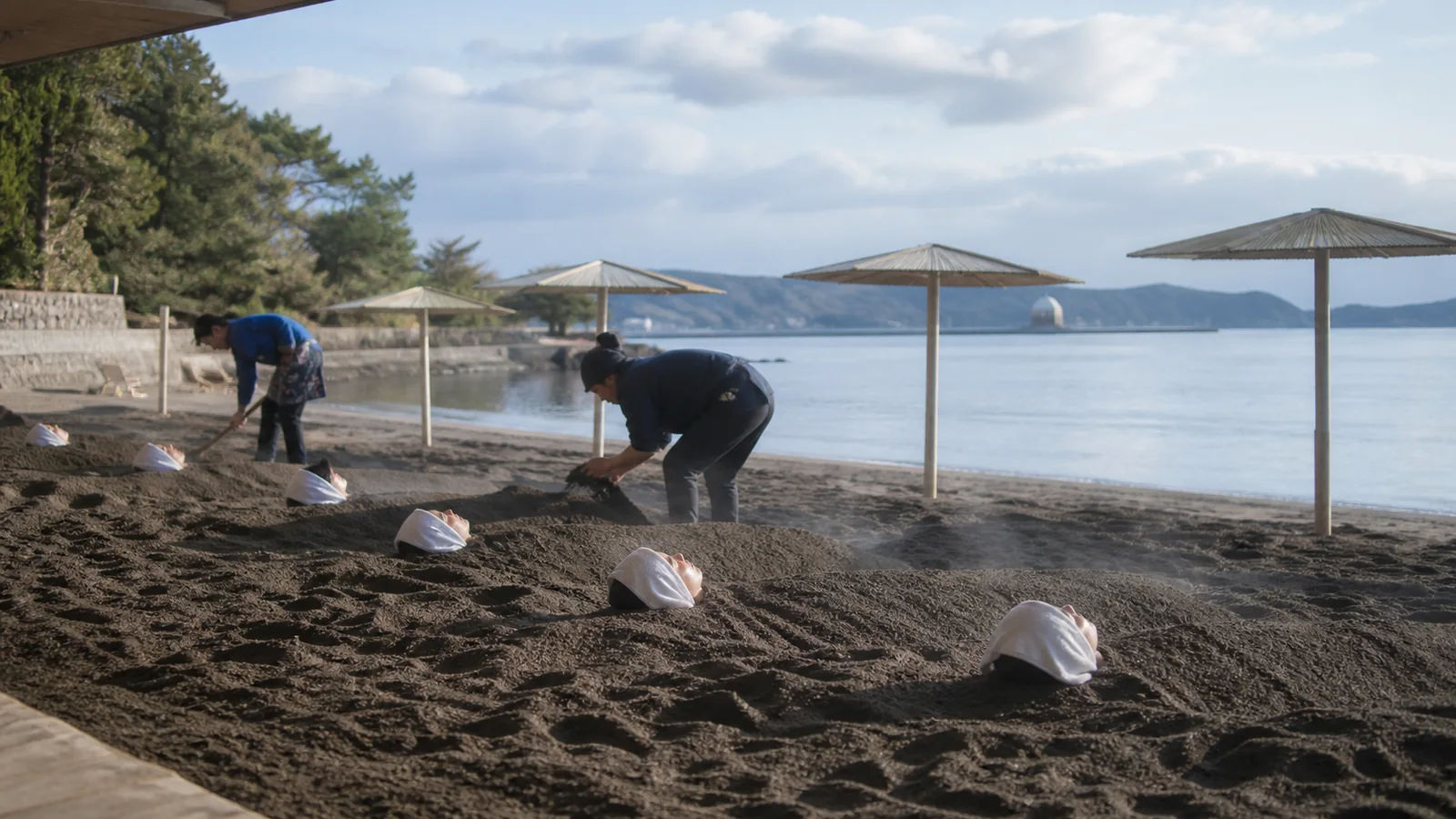 海辺の黒い砂に肩まで埋まって温まる砂むし温泉の利用者